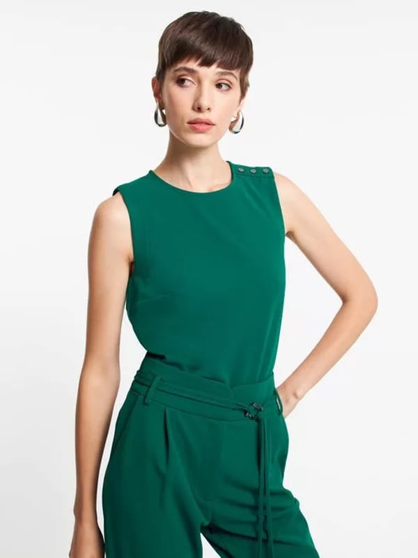 Blusas femininas para uniforme: modelo vestindo uma blusa de crepe sem manga com botões nos ombros verde.