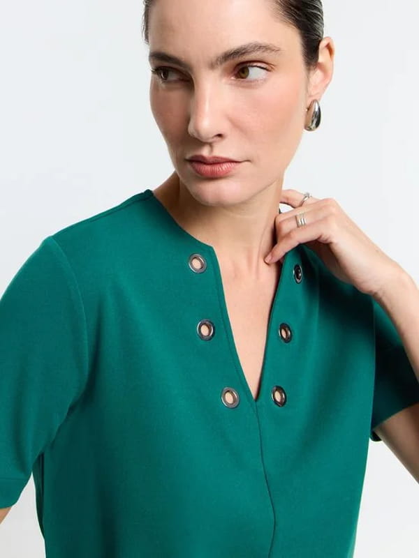 Blusa feminina de crepe: modelo vestindo uma blusa em crepe com decote V e detalhe de ilhoses verde - detalhes.