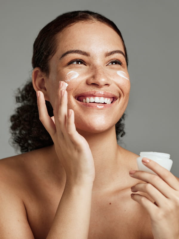 Como cuidar da beleza no verão: mulher passando creme hidratante no rosto.