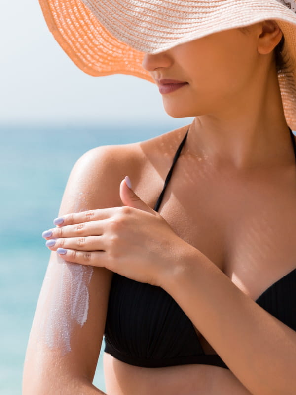 Como cuidar da beleza no verão: mulher passando protetor no corpo.