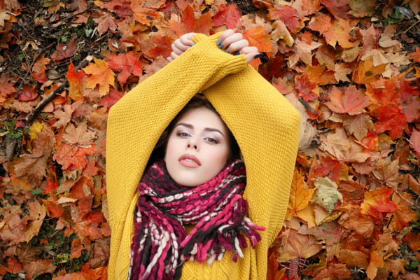 Saiba como se cuidar no inverno: mulher deitada sobre folhas coloridas de árvore.