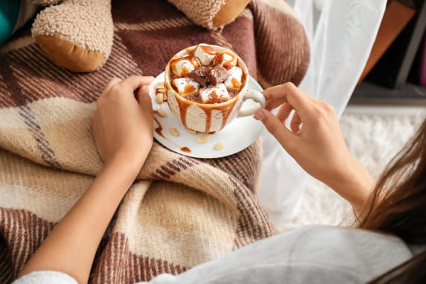 Saiba como se cuidar no inverno: mulher tomando uma xícara de café quente com desenhos personalizados.