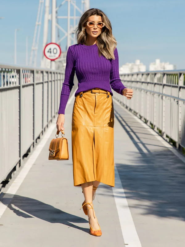 Cores que combinam com roxo: modelo vestindo uma blusa de tricot canelada roxa e saia amarela.