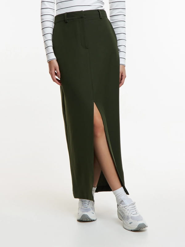 Look com saia midi e tênis: modelo vestindo uma saia midi em alfaiataria com fenda frontal verde - detalhes.