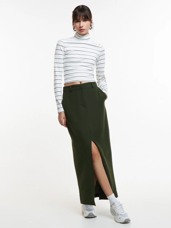 Look com saia midi e tênis: modelo vestindo uma saia midi em alfaiataria com fenda frontal verde.