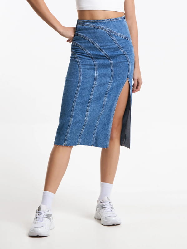 Look com saia midi e tênis: modelo vestindo uma saia midi jeans com recortes arredondados e fenda azul - detalhes.