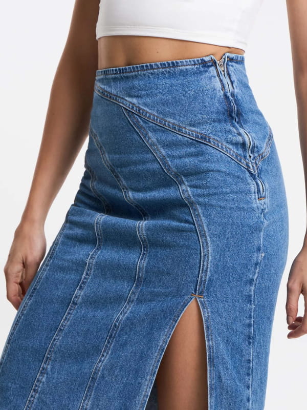 Look com saia midi e tênis: modelo vestindo uma saia midi jeans com recortes arredondados e fenda azul - fenda.