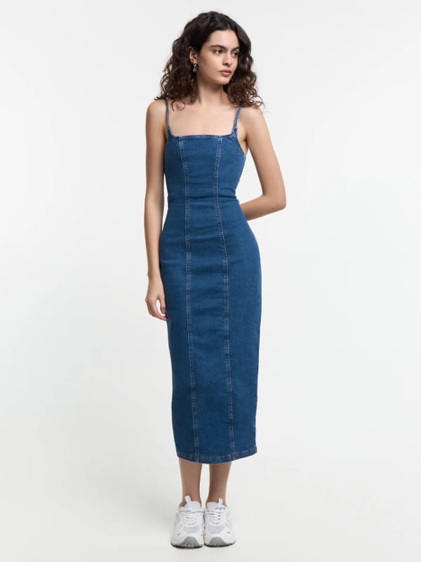 Como usar vestido midi com tênis: modelo usando um vestido midi jeans com modelagem justa e alcinhas reguláveis azul.